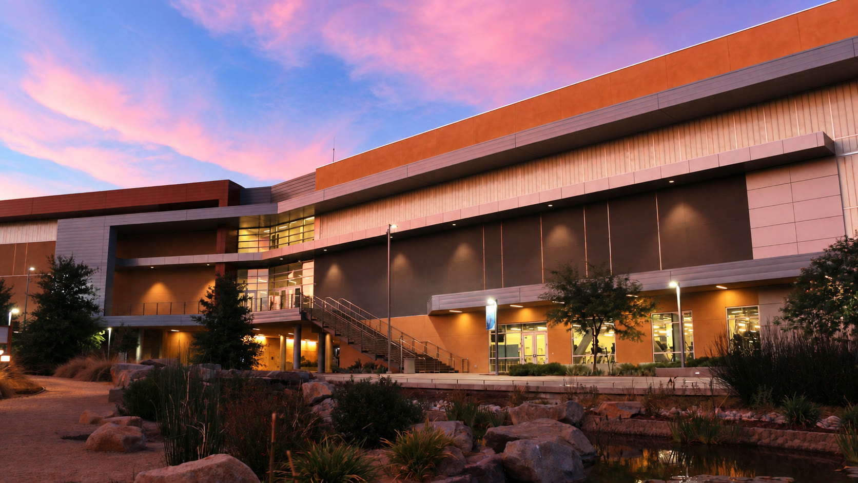 San Bernardino Valley College campus building lit at dusk, with a landscaped stream and walkways in the foreground.